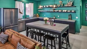 A modern kitchen with teal walls, a central island, and bar stools. - The Fish! Most Unique High-End Luxury Rental w/Private Pool On Folly Beach! (Charleston)