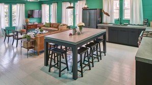 A modern kitchen with a central island, bar stools, and a dining area with a sofa and coffee table. - The Fish! Most Unique High-End Luxury Rental w/Private Pool On Folly Beach! (Charleston)