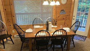 A wooden dining area with a table set for four, surrounded by chairs, a clock, and a sign above the table. - Adventure Awaits! (Snowshoe)