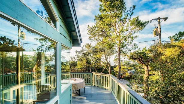 Une terrasse en bois avec une table et des chaises, entourée de rampes de verre et d’arbres.