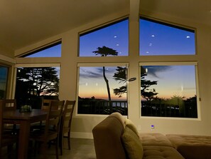 A room with large windows, a dining area with chairs and a table, and a sofa.