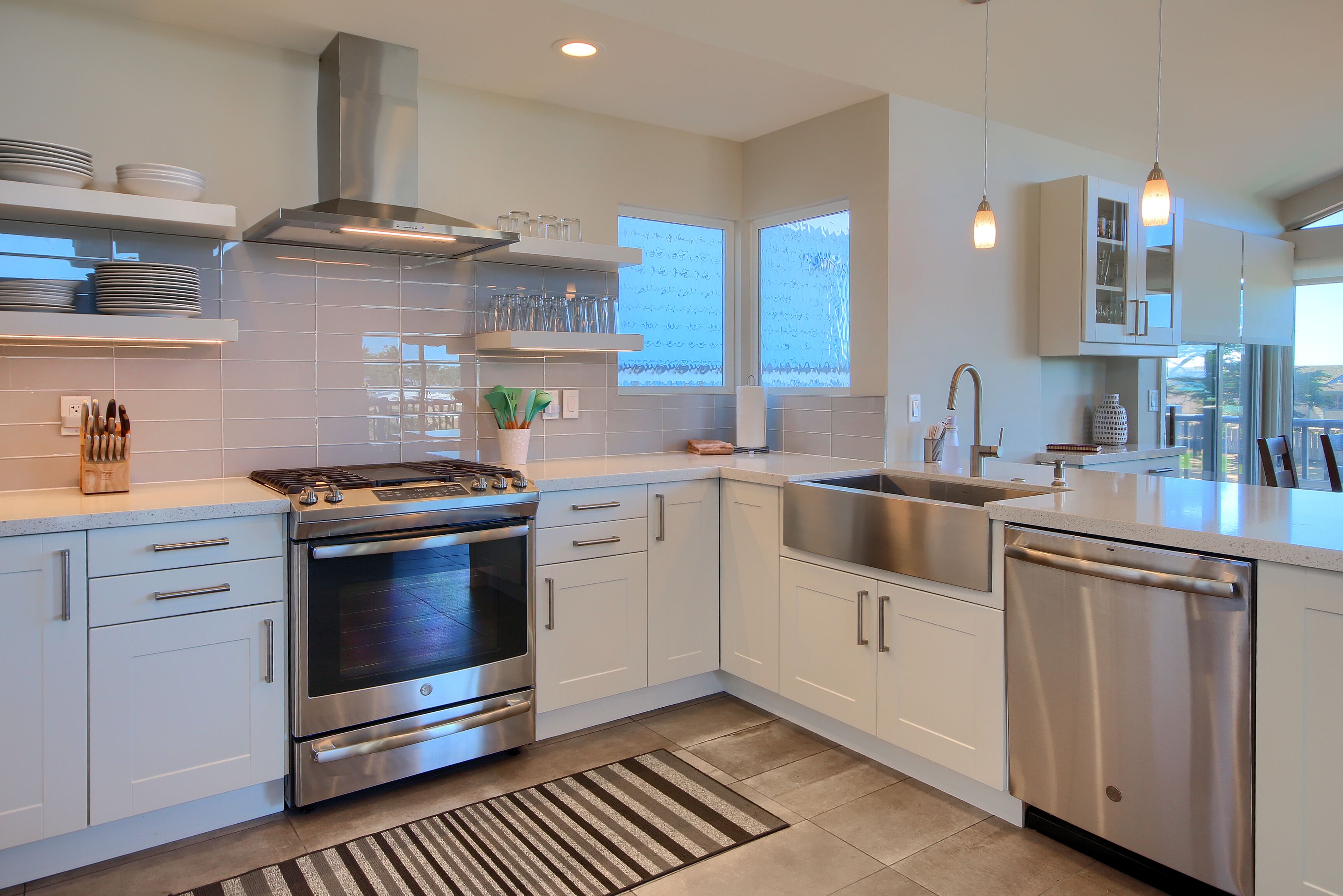 A modern kitchen with stainless steel appliances, white cabinetry, and a large window providing natural light.