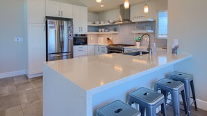 Een moderne keuken met witte kastjes, roestvrijstalen apparatuur en een centraal eiland met barkrukken.