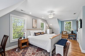 Quarto com cama grande, escrivaninha, cadeira, janela com persianas e ventilador de teto.