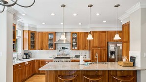 Una cocina con armarios de madera, una isla central con taburetes, electrodomésticos de acero inoxidable e iluminación colgante.