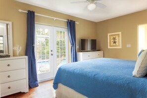 Een slaapkamer met een bed, een televisie, een dressoir en een deur naar een balkon.