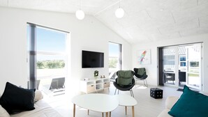 Un salon moderne doté d’une grande fenêtre, d’un téléviseur à écran plat, d’un canapé, d’une table basse et d’un fauteuil.