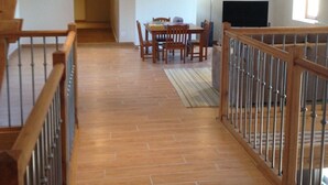A spacious attic room with a wooden staircase, a dining area with chairs and a table, and a television.