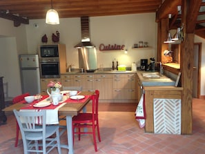 Una cocina compacta con armarios de madera, un extractor de acero inoxidable y un comedor con mantel rojo.