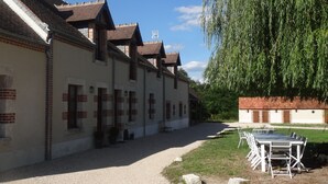 A building with multiple windows and a gravel path leading to a table and chairs set up outside.