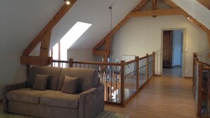 A loft-style room with a wooden ceiling, a sofa, and a view of the upper floor.