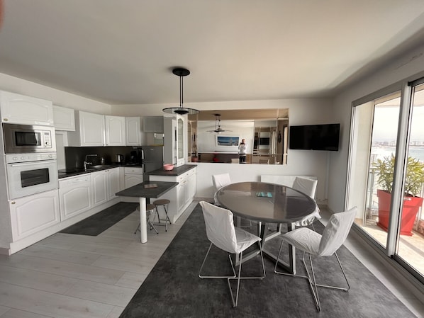 A modern kitchen with white cabinets, a dining area with a glass table and white chairs, and a large window offering a view of the city. - 2-bedroom apartment beachfront with parking, 3 stars (Les Sables-d'Olonne)