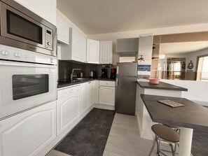 Una cocina moderna con muebles blancos, horno empotrado, microondas, cafetera y refrigerador.
