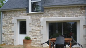 A stone house with a wooden deck, a dining table with chairs, and a potted plant. - Ty Bihan Small stone house in a quiet location 5 minutes from the beach (FOUESNANT)