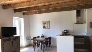 A modern kitchen with a dining area, wooden ceiling beams, a television, and a painting on the wall. - Ty Bihan Small stone house in a quiet location 5 minutes from the beach (FOUESNANT)