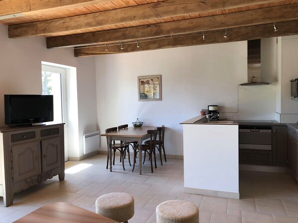 A modern kitchen with a dining area, wooden ceiling beams, a television, and a painting on the wall.