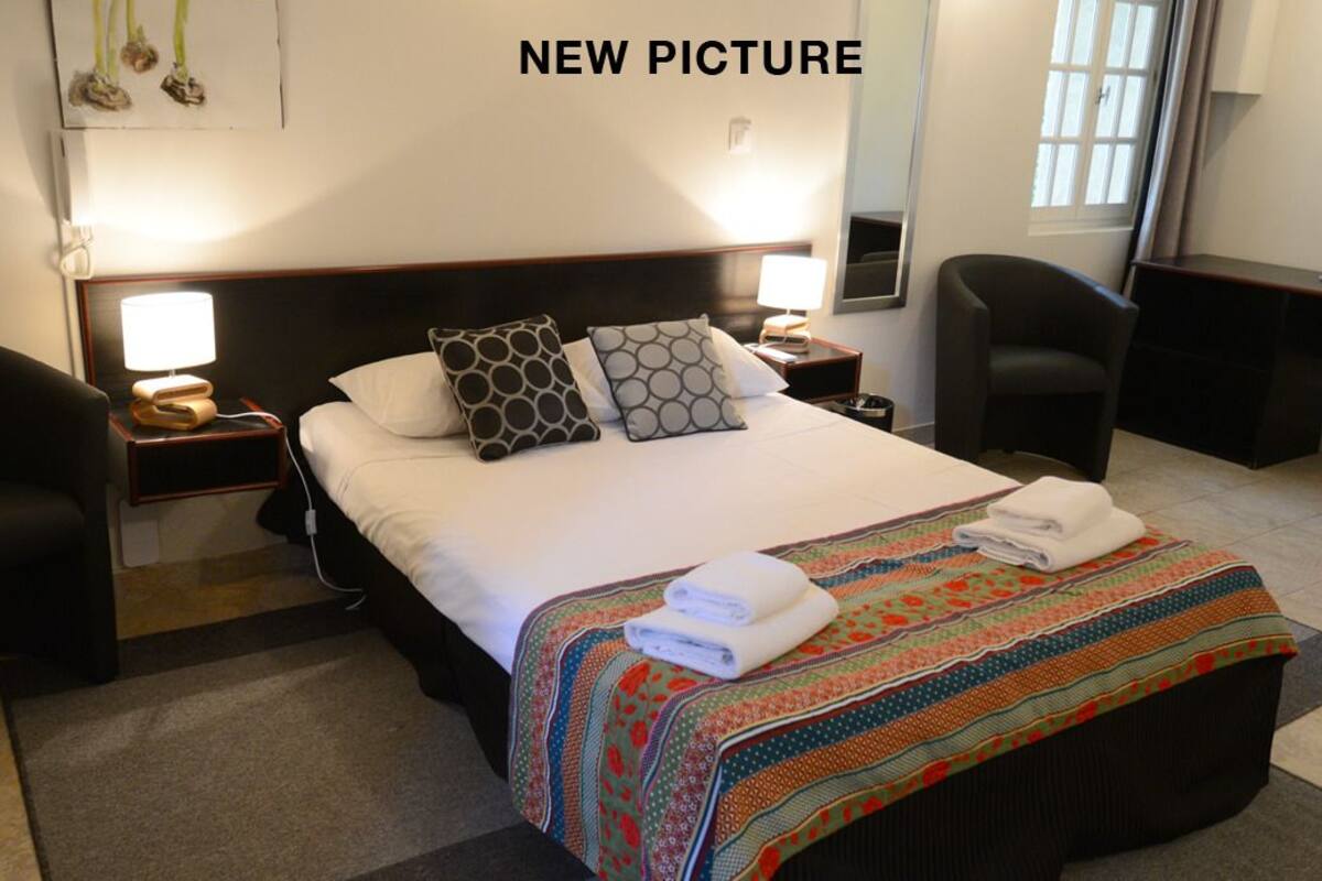 Een opgemaakt bed met gestreepte kussens, een kleurrijke quilt en twee bedlampjes.