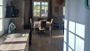 Ett modernt kök med diskho, matbord och stolar, som leder vidare till en matplats med utsikt över grönområden.