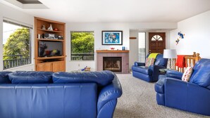 A living room with blue leather sofas, a wooden entertainment unit, a fireplace, and a door leading to another room. - Snug Harbor: 3  BR, 2  BA House in CAMBRIA, Sleeps 6 (CAMBRIA)