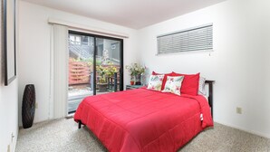 A bedroom with a red bedspread, a sliding glass door to a balcony, and a small potted plant on the nightstand. - Snug Harbor: 3  BR, 2  BA House in CAMBRIA, Sleeps 6 (CAMBRIA)
