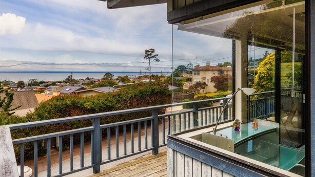 A balcony with a glass enclosure overlooking a residential area with houses and a body of water. - Snug Harbor: 3  BR, 2  BA House in CAMBRIA, Sleeps 6 (CAMBRIA)