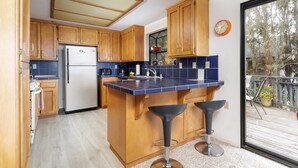 A compact kitchen with wooden cabinets, a built-in refrigerator, a blue countertop, and a small bar area with stools. - Snug Harbor: 3  BR, 2  BA House in CAMBRIA, Sleeps 6 (CAMBRIA)