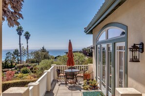 A patio with a table and chairs, a red umbrella, and a view of the ocean. - Oceanview Gatsby House (Cambria)
