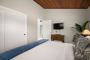 A bedroom with a bed, a dresser, a television, and a plant.