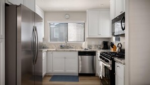 A modern kitchen with white cabinets, stainless steel appliances, a clock, and a window with blinds. - Sea'Scape : 2  BR, 2  BA House in Cambria, Sleeps 4 (Cambria)