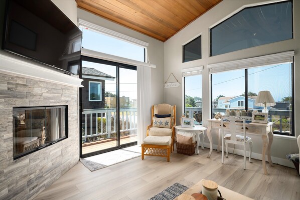 A spacious living area with a fireplace, large windows, and a balcony. - Sea'Scape : 2 BR, 2 BA House in Cambria, Sleeps 4 (Cambria)