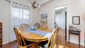 A dining area with a wooden table, chairs, and a chandelier. There are paintings on the wall and a small table with decorative items.