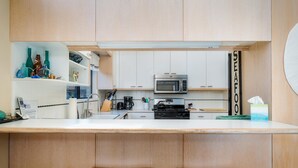 Une cuisine moderne avec des armoires blanches, un four à micro-ondes en acier inoxydable et une machine à café. On y trouve deux tabourets noirs près du comptoir.