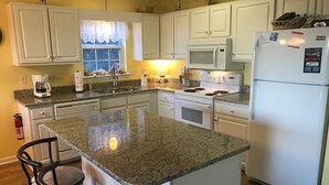 A kitchen with white cabinets, a granite countertop island, a microwave, a stove, and a refrigerator. - Great Ocean View! Quiet Cul-de-sac, 4 minute walk to Beach, Waterpark, Shopping  (Emerald Isle)