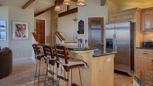 A kitchen with a central island, bar stools, a refrigerator, and wooden cabinetry. - Bristol By the Sea: 3  BR, 3  BA House in Cambria, Sleeps 8 (Cambria)