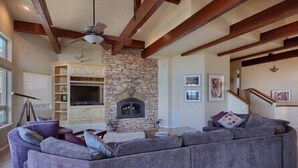A living room with a stone fireplace, a large gray sectional sofa, and a ceiling fan. - Bristol By the Sea: 3  BR, 3  BA House in Cambria, Sleeps 8 (Cambria)
