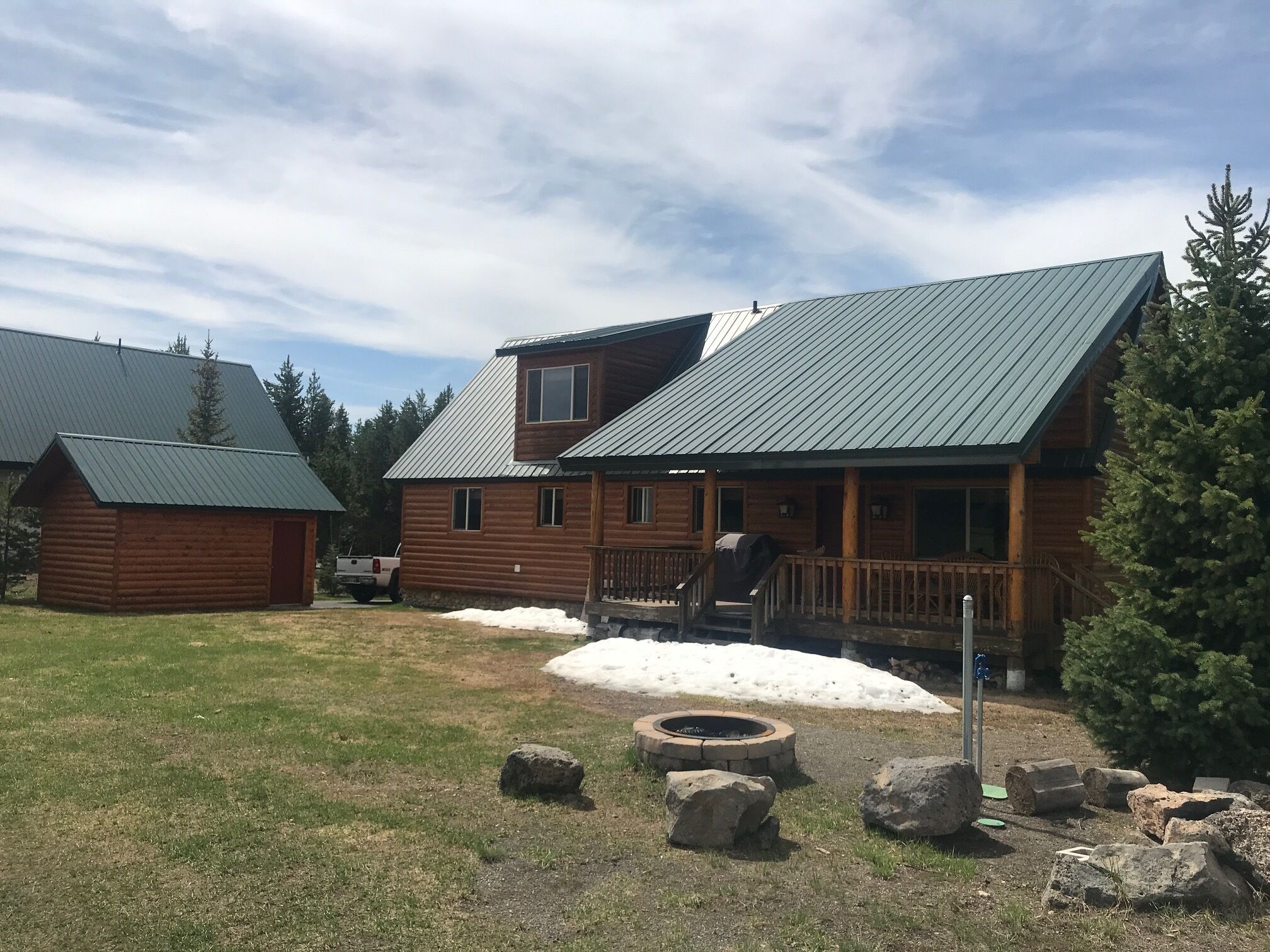 A log cabin with a metal roof, a porch, and a fire pit in the yard.