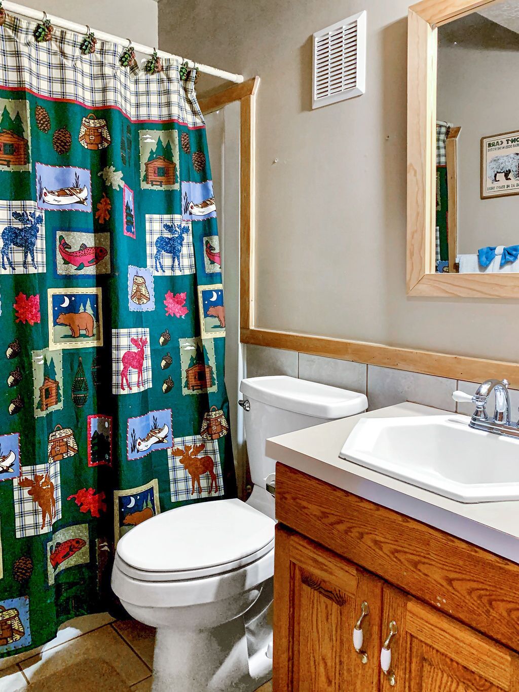 A bathroom with a white toilet, wooden vanity, and a green shower curtain with wildlife patterns.