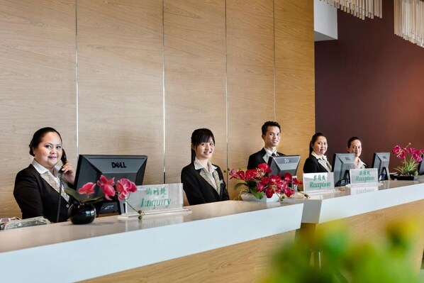 A reception desk with staff members seated behind it, each with a nameplate and a computer monitor.