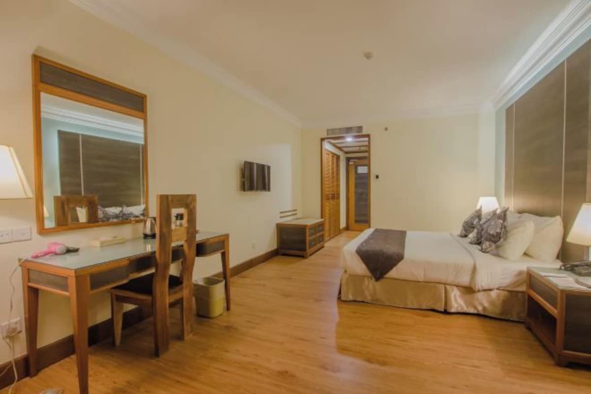 Una habitación de hotel con un escritorio de madera, una cama con almohadas, un espejo y un televisor.