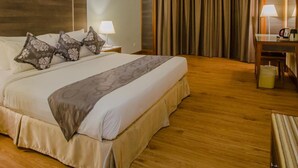 Una habitación de hotel con una cama grande, un escritorio con silla, una lámpara y una cortina.