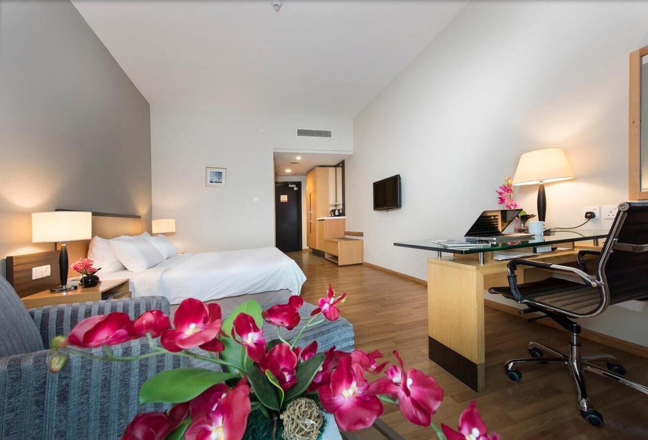 Una habitación de hotel con cama, escritorio, silla, televisión y una pequeña mesa con lámpara.