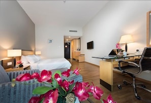 Una habitación de hotel con cama, escritorio, silla, televisión y una pequeña mesa con lámpara.