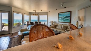 A spacious living room with a large window overlooking the ocean, a comfortable sofa, and a dining area with a table.