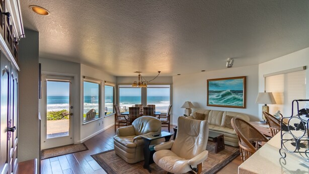 A spacious living room with a view of the ocean, a large painting, and a dining area with wicker furniture.