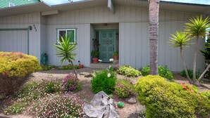 A house with a green door, a small garden with various plants and flowers, and a palm tree. - A Cool House, A Cool View (Cambria)