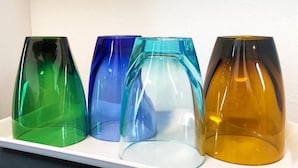 Uma prateleira branca com quatro vasos de vidro de cores diversas.