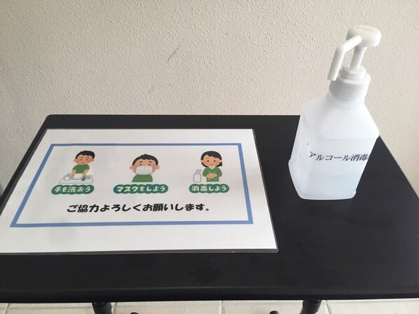 Una mesa con dispensador de gel hidroalcohólico y un cartel con ilustraciones y texto en japonés.