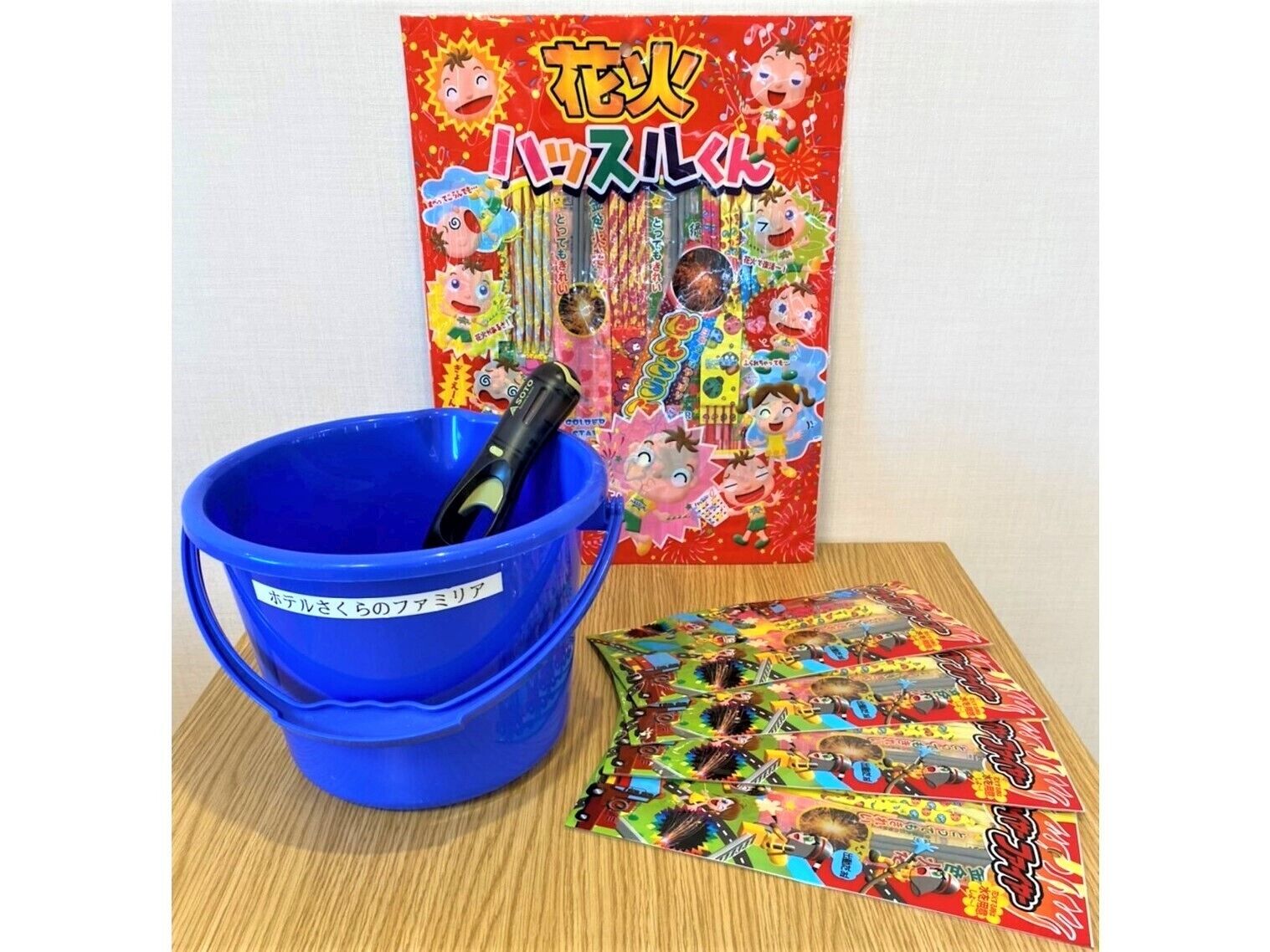 A blue bucket with a pen, a colorful card game, and a Japanese book titled "花火 ハッピー".