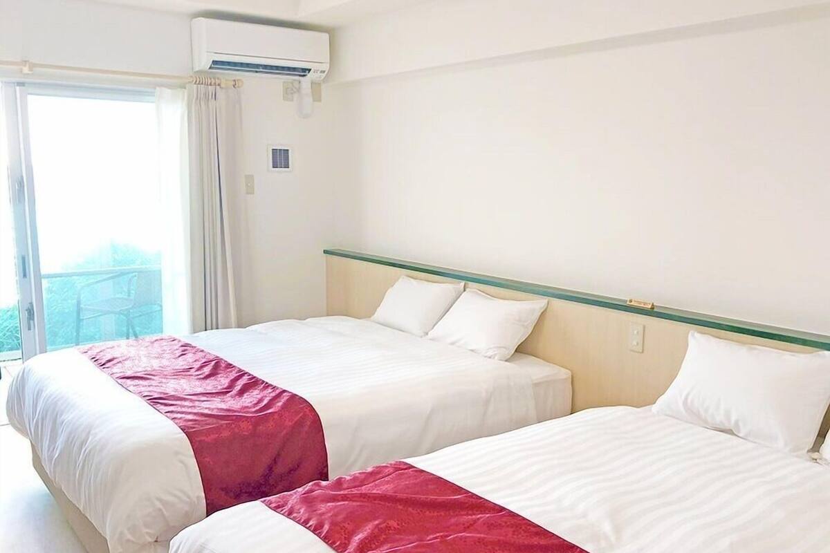Habitación de hotel con dos camas, una ventana con cortinas, un equipo de aire acondicionado y un ventanal pequeño.
