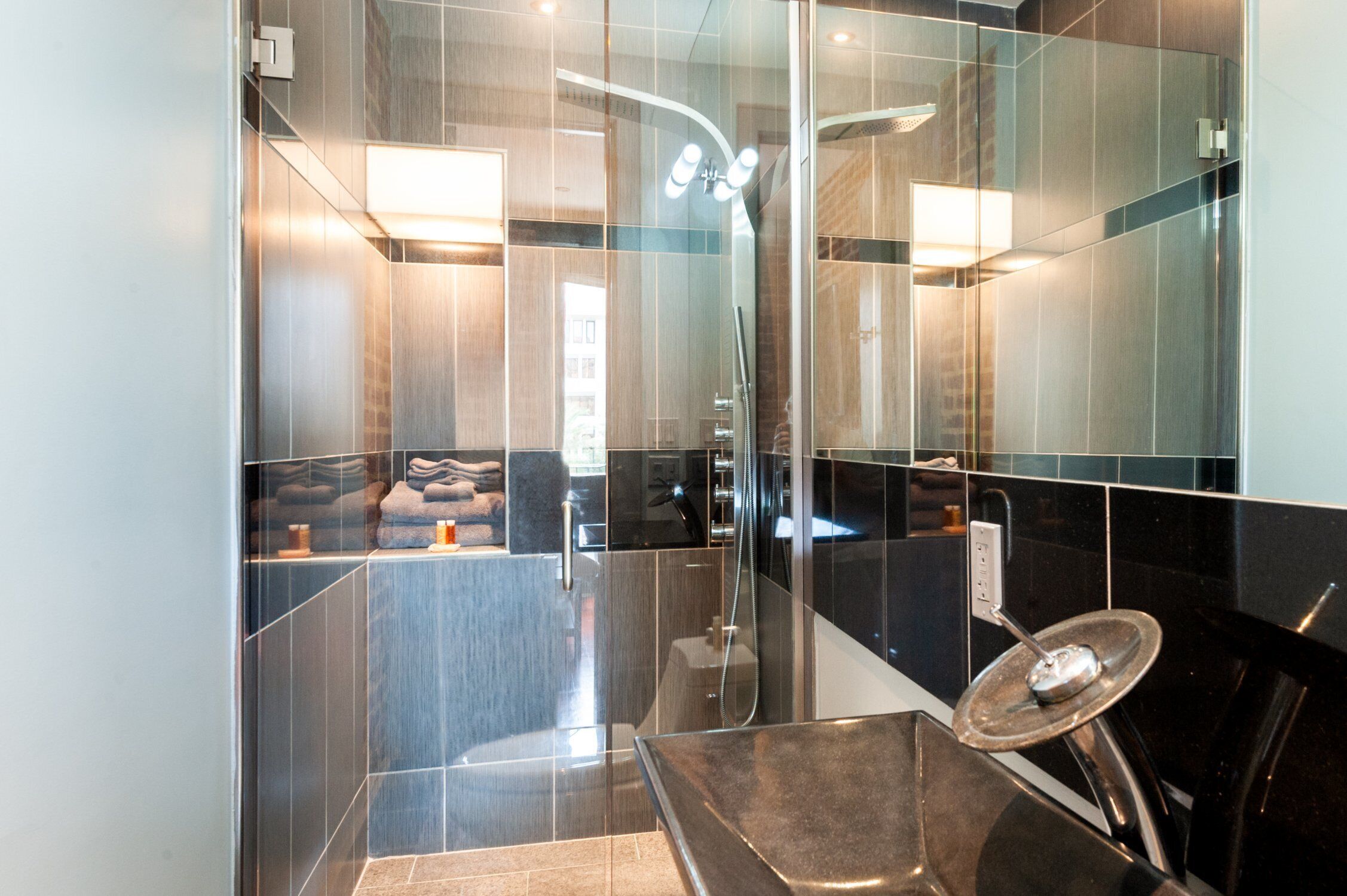 Une salle de bain moderne avec une douche à parois de verre, un lavabo noir et un miroir.